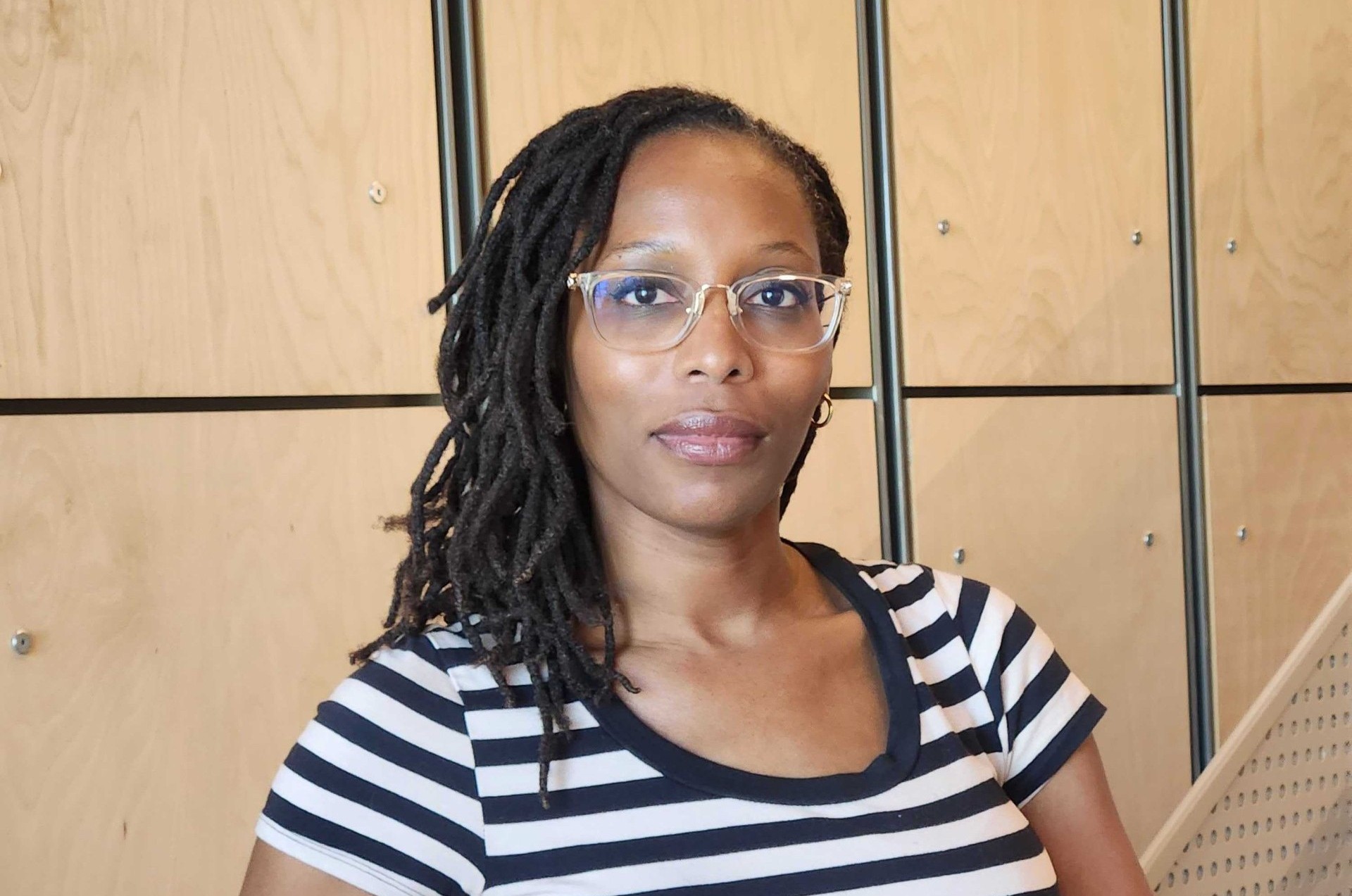 A headshot of Carla LynDale Bishop. She is a Black woman with long locs. She is wearing a cotton-stripped dress.