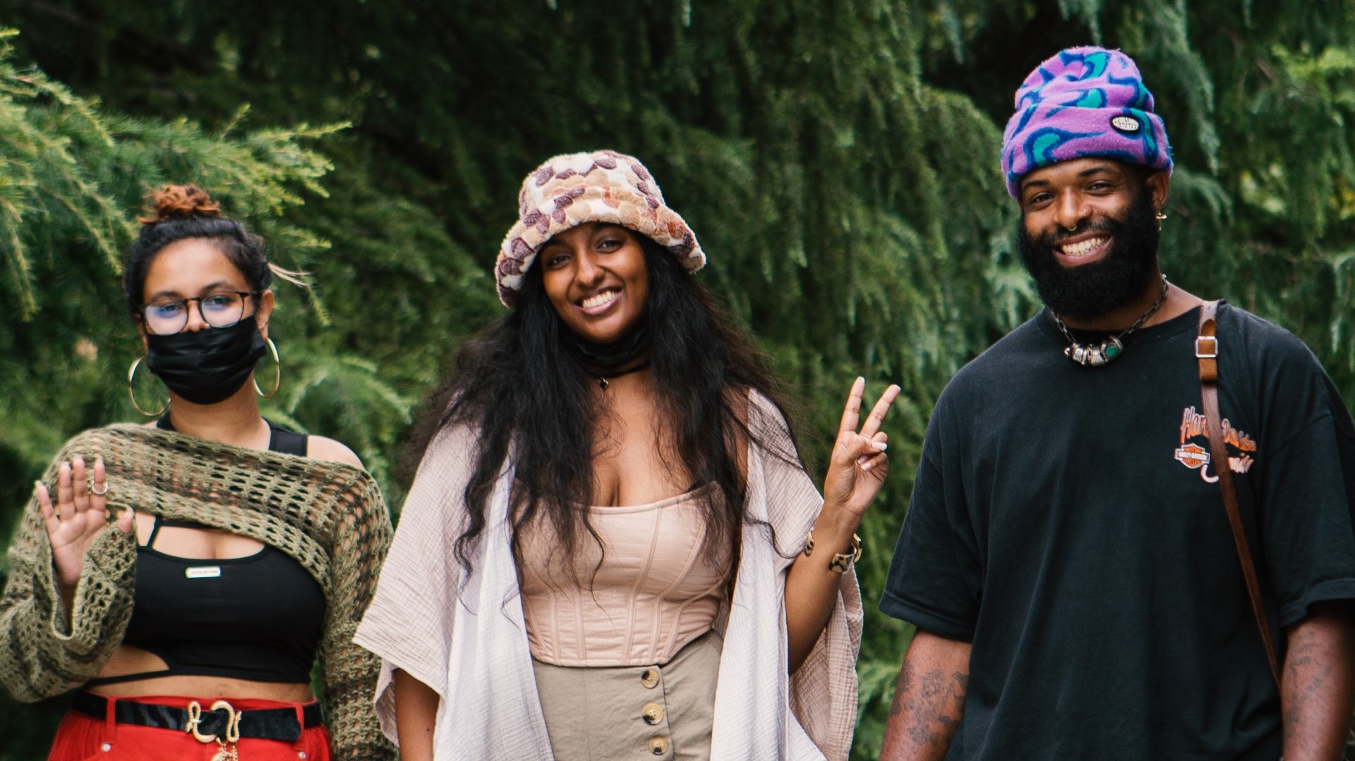 Three people pose for the camera as they approach the 2023 BlackStar Film Festival. The two on the right are smiling brightly and all are dressed fashionably, with the person in the middle holding up a peace sign. The person on the far left is masked and waving at the camera.