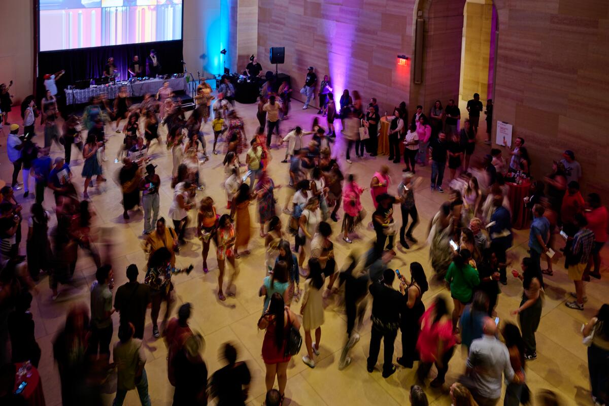 A photo of a large room in the Philadelphia Museum of Art, it is filled with people dancing. There is a DJ booth at the far end.