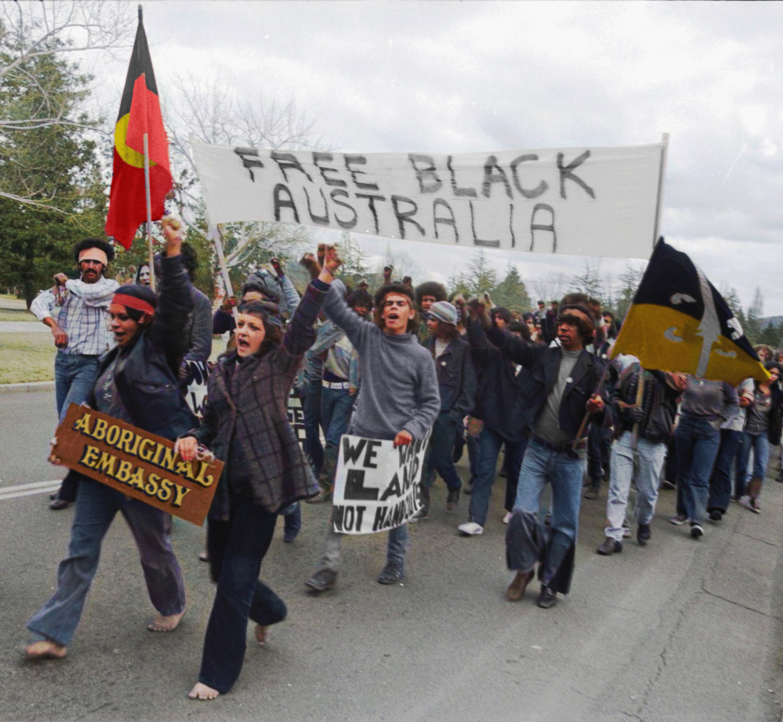 A still from Still We Rise shows a a group of protesters marching, many are holding their fists in the air, some are carrying signs that read "Free Black Australia" and "Aboriginal Embassy."