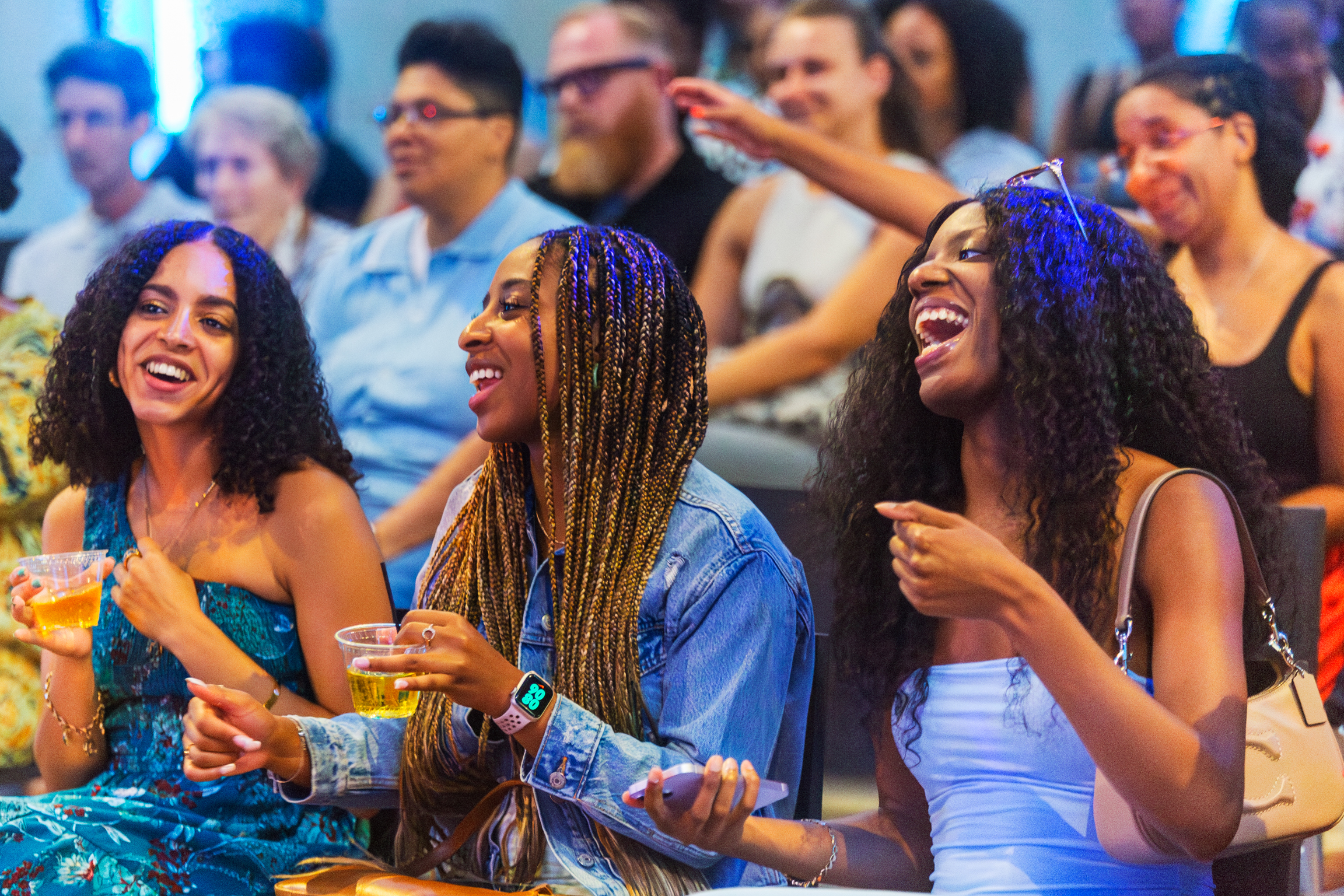 Three Black people laugh in joy while sitting and watching something