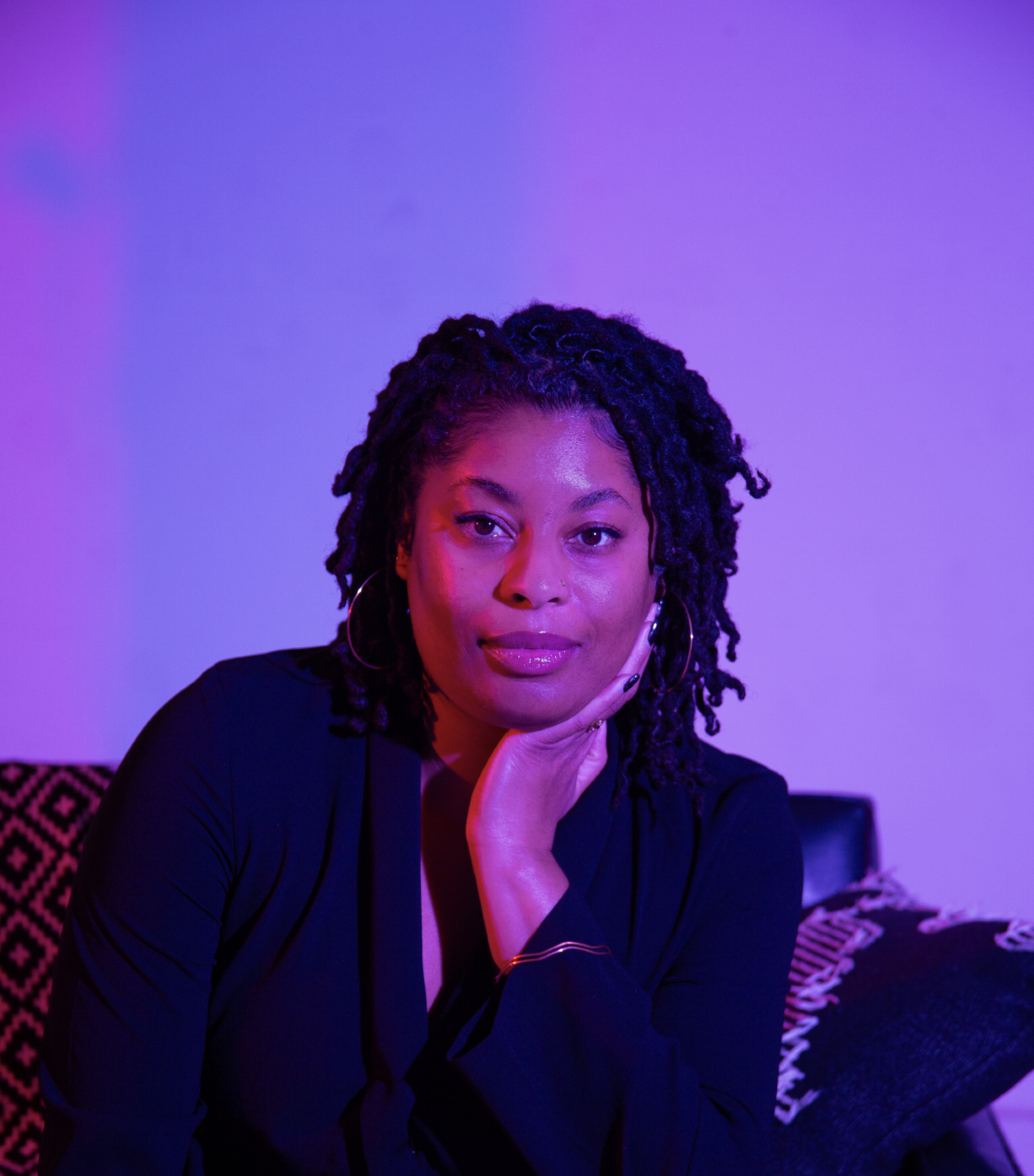 A headshot of Yasmine Espert, they are a Black non-binary person. They have locs and are smiling softly at the camera.