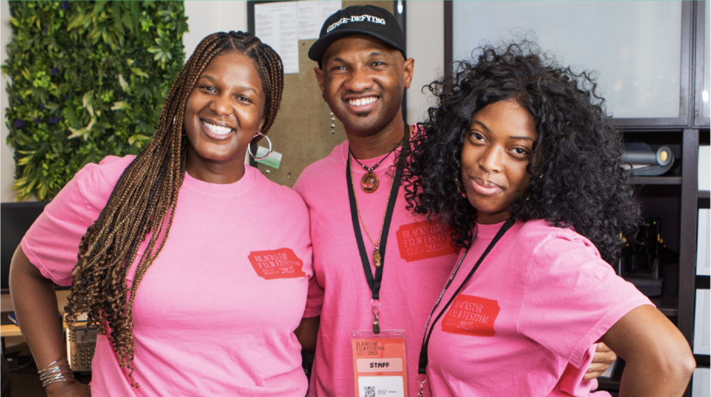 A photo of three BlackStar Film Festival employees standing arm-in-arm and smiling. They all have on pink BlackStar Film Festival t-shirts.
